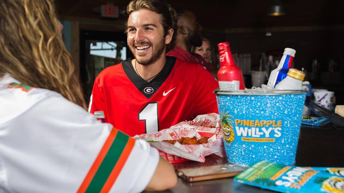 Close up of a guy and girl sitting at a bar with a bucket of beer branded Pineapple Willy's and a basket of wings next to them at Pineapple Willy's in Panama City, Florida, USA